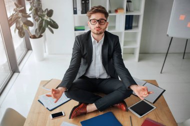 Toplantı salonunun içinde tablo üzerinde meditasyon sakin huzurlu genç adam. O sit bacaklar ile sakin ve huzurlu geçti. Malzeme ve masada her yerde malzemeleri