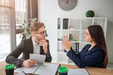 Düşünceli genç adam ve kadın birlikte beyaz odada pencerede çalışır. Model açıklamak ve el ile göstermek. Adam bak ona. Takım çalışması.