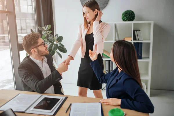 Ung kvinna stå och introduceras till kille av en annan kvinna. De alla är i konferensrum. Brunette titt på blond kvinna. Två personer skakar hand. — Stockfoto