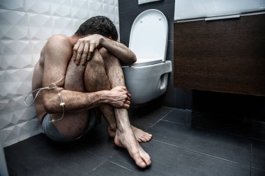 Uyuşturucu bağımlılığı ile yalnız kırık adam yerde tuvalet dinlenme odasında oturmak. Acı. Soluk cilt ve ince zayıf beden. El örgü ile sarılır. Duygusal tükenme.