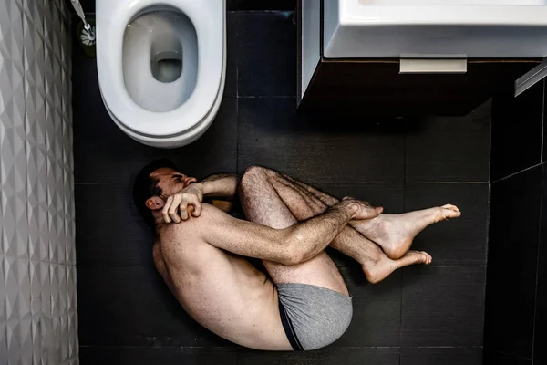 외로운 젊은이 혼자 화장실에서 내부 고통. 그는 바닥에 누워 하 고 손으로 다리를 잡고. 남자 착용만 반바지. 화장실의 열린된 가기입니다. 고 통과 중독. — 스톡 사진