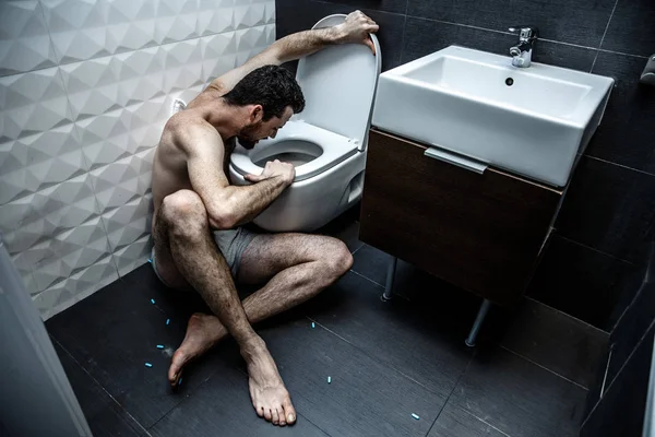 Sjukt blek ung sitta på golvet i vilorum på toaletten. Han ser ut inuti. Killen kommer att rapa. Bed känslor och fruktansvärda problem. — Stockfoto