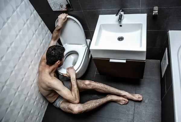 Jovem solitário e doente, de mãos dadas na sanita. Senta-se na sala de descanso. Um tipo nu. Ele vai arrotar. Illnes e fraco . — Fotografia de Stock