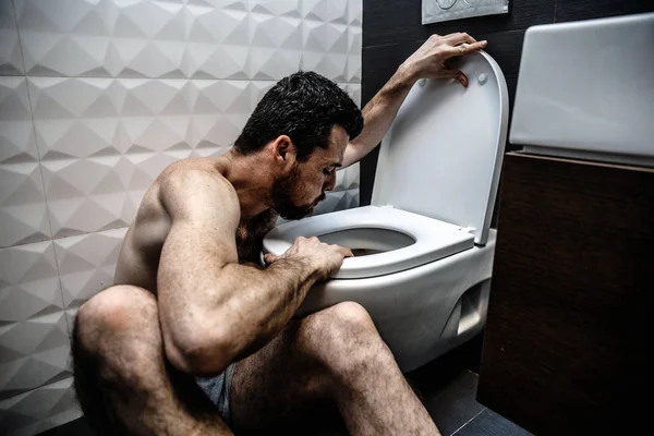 Un joven se sienta en el baño y eructa en él. Enfermedad y debilidad. Se sienta solo en el cuarto de descanso frío. Agotamiento y mala reacción . — Foto de Stock