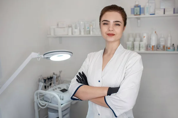 Joven esteticista profesional de pie en la sala de cosmetología y posar en cámara. Ella tiene hads cruzados. Modelo mirada confidente . — Foto de Stock