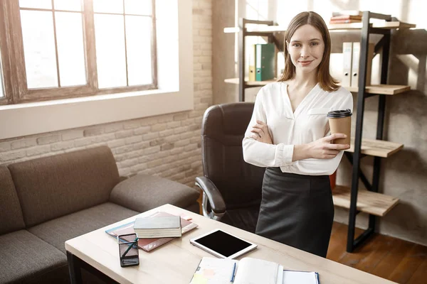 Kendine güvenen güzel genç buisnesswoman odasında. Kamera ve poz bul. Model kahve tutun. O gülümseme.