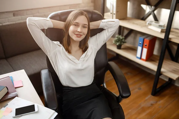 Young woman having break during workday. She hold hands behind head and smile. she Sit in room. — Stock Photo, Image