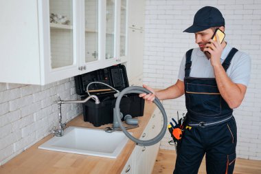 Genç tesisatçı mutfak lavabo, telefonda konuşuyor. O hortum tutun. Reparing. Araç üstünde okul sırası. Gün ışığı.