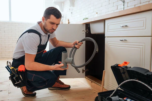 Hoch konzentriert sitzen junge Arbeiter in Kaderpose in der Küche. er hält ein Stück Pfeife und Hoffnung. Typen, die Reparatur machen. Werkzeugkiste auf dem Boden geöffnet. — Stockfoto