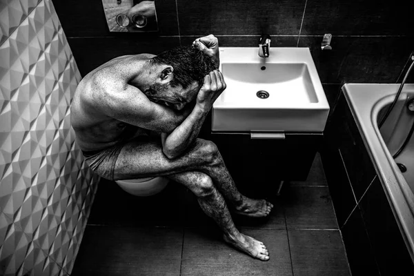 Hombre desnudo sentado en el baño de la vieja ciudad. La persona siente terrible dolor emocional e impotencia. El adicto se siente mal. Imagen en blanco y negro . — Foto de Stock