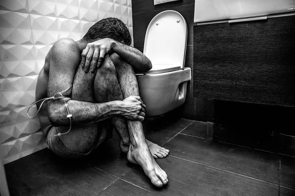 Hombre solo roto con adicción a las drogas sentarse en el suelo en el cuarto de baño en el baño. Sufre. La mano está envuelta con trenza. Agotamiento emocional. Imagen incolora en blanco y negro . — Foto de Stock