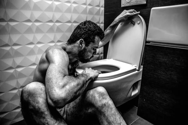 Jongeman zit op toilet en burp erin. Ziekte en zwak. Hij zit in koud Rustlokaal alleen. Uitputting en slechte reactie. Zwart-wit foto. Kleurloos. — Stockfoto