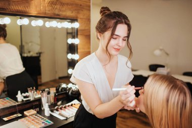 Genç kadın yapmak kadar koyarak ve sarışın model yüzündeki kaptırdın. O güzellik salonunda onun önünde ayakta durmak. Doğru ve konsantre