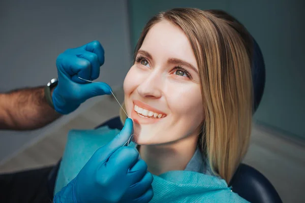 Mujer joven sentarse en la odontología en silla y mirar hacia arriba. El médico usa hilo dental para limpiar Ella sonríe y muestra hermosos dientes . — Foto de Stock