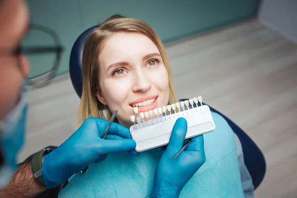 Médico varón de pie sobre el cliente y poner dientes artificiales a los verdaderos. Procedimiento de blanqueamiento o sustitución de dientes. La cliente se sienta en la silla y mira hacia arriba. Ella muestra sus dientes blancos . — Foto de Stock