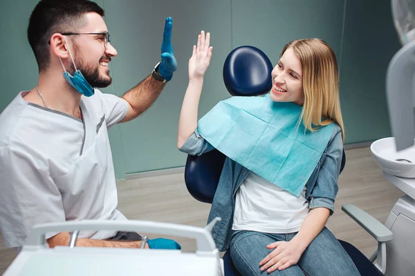 Young cheerful client and dentist giving high-five to each other in dentistry. They smile. Work is done. — Stock Photo, Image