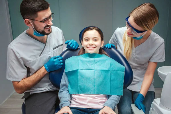 El dentista positivo cuidadoso del varón y de la mujer mira al paciente del cabrito y sonríe. Niña sentada en silla dental. Se ve recta y sonríe. Aislado sobre fondo verde . — Foto de Stock