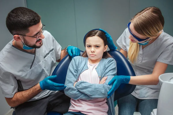 Fille têtue s'asseoir dans cair ddental dans la chambre. Les dentistes la regardent inquiète. Ils la touchent et lui parlent. Isolé sur fond vert . — Photo