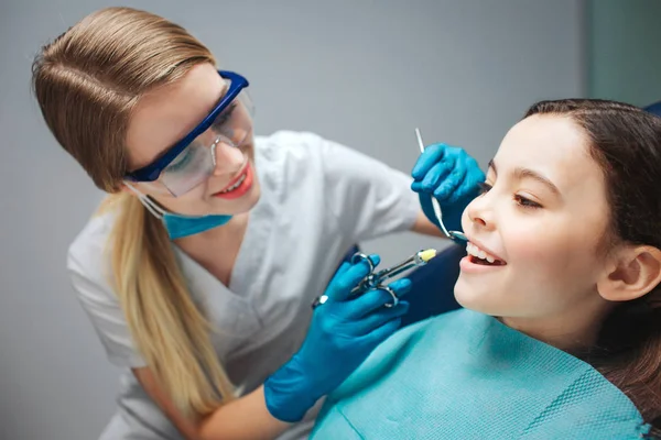 Dentista femenino cuidadoso mantenga las herramientas cerca de la boca de la chica. Muestra los dientes delanteros. Se sienta tranquilamente en la silla dental. . — Foto de Stock