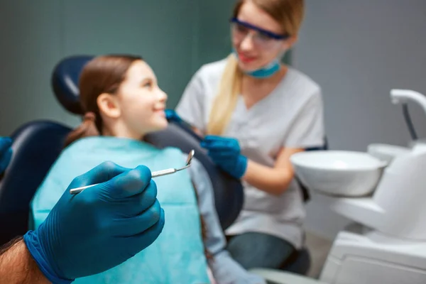 Main dans la tenue de gant en latex outil dentaire tenir outil dentaire. Enfant assis sur la chaise et sourire à la femme. Une dentiste se tient à côté . — Photo