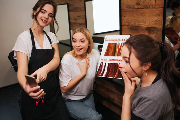 Sorprendió a las mujeres jóvenes mirando el teléfono mientras la peluquera lo sostenía en la mano. Peluquero propone la coloración de pelo de moda en el salón —  Fotos de Stock