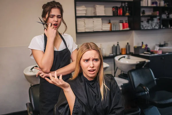 Angry blonde young female client screaming at hairdresser as a haircut done bad. Fight in beauty salon