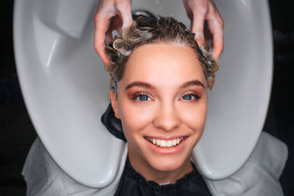 Top view of happy female customer smiling while hairdresser massaging hair. Young woman resting in beauty salon