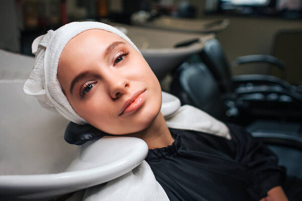 Close-up of beautiful relaxed woman with towel on head looking at camera after professional hair washing. Hair care in beauty salon