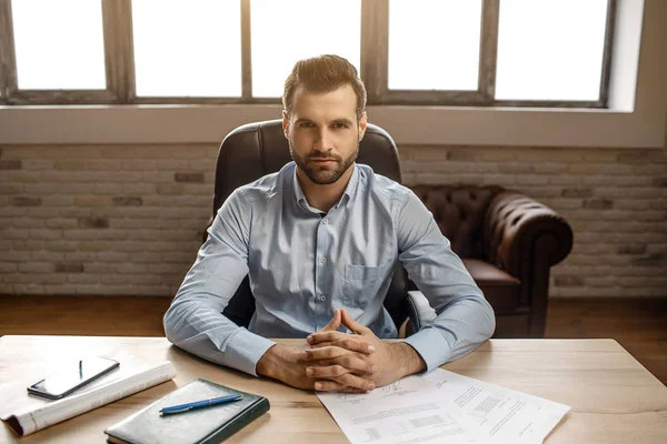 Genç yakışıklı işadamı masaya oturup kendi ofisinde poz. Doğrudan kameraya bak. Defter günlük ve telefon Danışma.