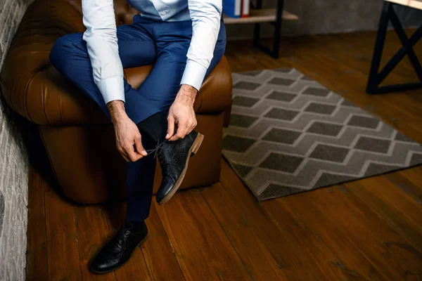 Cut view of young handsome businessman in his own office. He hold leg on another one and tie laces on shoes. Busy. — Stock Photo, Image