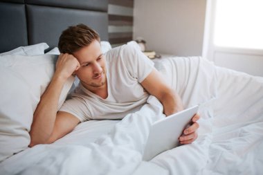 Bu sabah yatakta rahat huzurlu genç adam. O beyaz tablet tutun. Göz ve bu adam ve gülümse. Baş taraftan dostum. Sakin ve huzurlu.