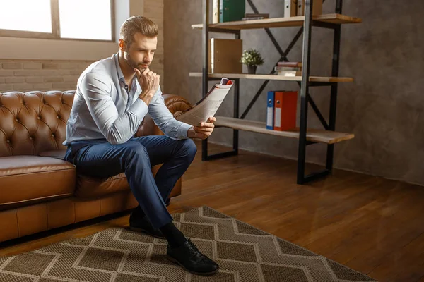 Genç yakışıklı düşünceli işadamı oturun ve kendi ofisinde günlüğü okuyun. O poz. Kendinden emin ve seksi. Gün ışığı.