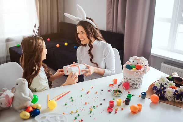 Mutter und Tochter bereiten sich im Zimmer auf das Osterfest vor. junge Frau hält Geschenk in Händen für Mädchen. sie schaut sie an und lächelt. Mädchen glücklich. — Stockfoto