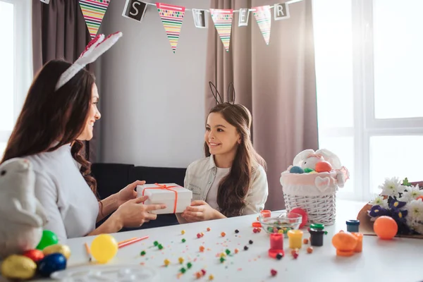 Mama și fiica se pregătesc pentru Paști într-o cameră minunată. Ei sunt prezenți împreună. Femeia și fetița se uită unul la celălalt și zâmbesc. Decorarea și ouăle pe masă . — Fotografie, imagine de stoc