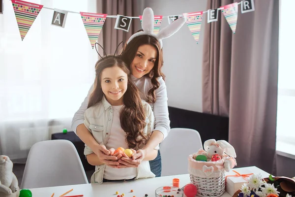 Mutter und Tochter verbringen Ostern im Zimmer. stehen sie und halten bunte Eier in den Händen. Die Leute schauen in die Kamera und lächeln. Festlich und glücklich. — Stockfoto
