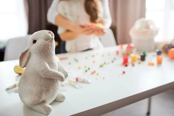 母女俩站在房间里为复活节做准备。白色兔子玩具站在桌子上。装饰和糖果后面。节日。特写. — 图库照片