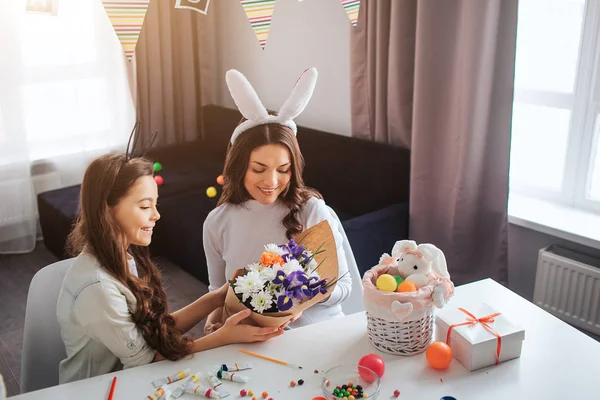 Mutter und Tochter bereiten sich auf Ostern vor. Mädchen geben schönen Strauß an ihre Mutter. Osterdekoration Süßigkeiten und Farbe auf dem Tisch. — Stockfoto