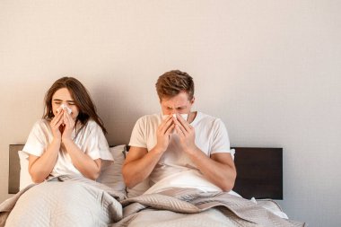 Genç çift yatakta. Hasta erkek ve kadın burun üfleme ve hasta yatak odasında acı