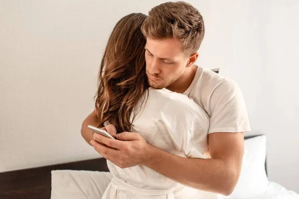 Jong koppel in de slaapkamer. Een aantrekkelijke man is het controleren van inkomende berichten in de ochtend — Stockfoto