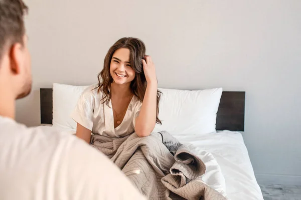 Casal jovem na cama. Sorrindo bela mulher faminta está esperando por um delicioso café da manhã — Fotografia de Stock