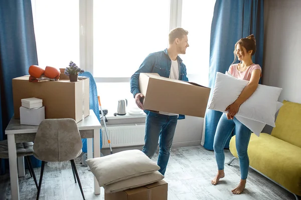 Ung familj par köpt eller hyrt sin första lilla lägenhet. De står i rummet med box och kuddar. Människor ser på varandra. — Stockfoto