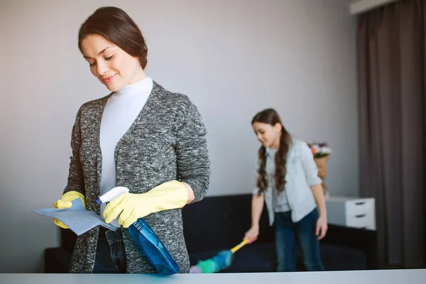 Piękna Brunetka kaukaski matka i córka razem sprzątanie w pokoju. Młoda kobieta spray na gąbkę. Dziewczyna stoją za i blust kurz. — Zdjęcie stockowe