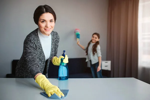 Linda morena caucasiana mãe e filha limpeza juntos no quarto. Jovem alegre lavando a mesa e segure o spray. Menina ficar atrás e blust o pó . — Fotografia de Stock