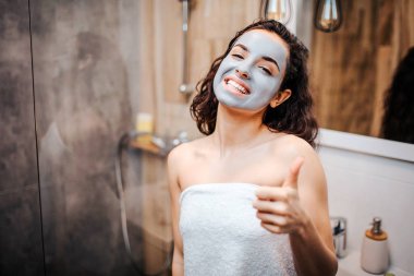 Sabah akşam rutin ayna adlı genç sportif esmer güzel kadının yapması. Neşeli mutlu modeli göz kamera ve msile. O yüz maskesi vardır. Kadın büyük başparmak bekle.