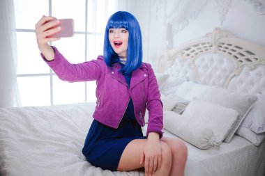 Moda ucube. Glamour mutlu güzel mavi saçlı ve modaya uygun makyaj holding bilgisayar ve yatakta otururken selfie yapıyor kadındır. Moda ve güzellik kavramı.