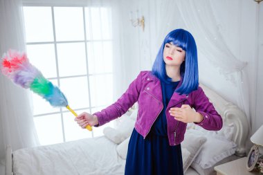 Moda ucube. Glamour sentetik kız, beyaz yatak odasında temizlik süpürme ile boş bakmak ve mavi saç sahte bebek tutuyor. Mor ceket şık güzel kadın. Moda ve güzellik kavramı