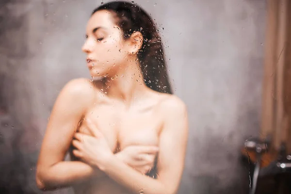 Young attractive sexy woman in shower. Blurred picture. Drk hailred model cover her breast with hands and looking to side. Eyes closed. Posing. — Stock Photo, Image