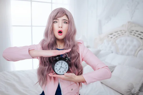 Monstruo de moda. Glamour mujer hermosa emocional con el pelo largo lila está sosteniendo reloj negro mientras está sentado en el dormitorio blanco. Concepto de belleza y moda . —  Fotos de Stock