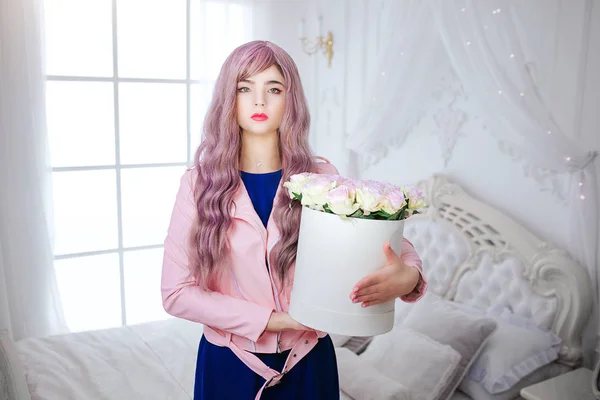 Modefreak. Glamour-Synthetikmädchen, falsche Puppe mit leerem Blick und langem fliederfarbenem Haar hält Schachtel mit Blumen, während sie im weißen Schlafzimmer steht. stilvolle schöne Frau in blauem Kleid. Schönheitskonzept — Stockfoto