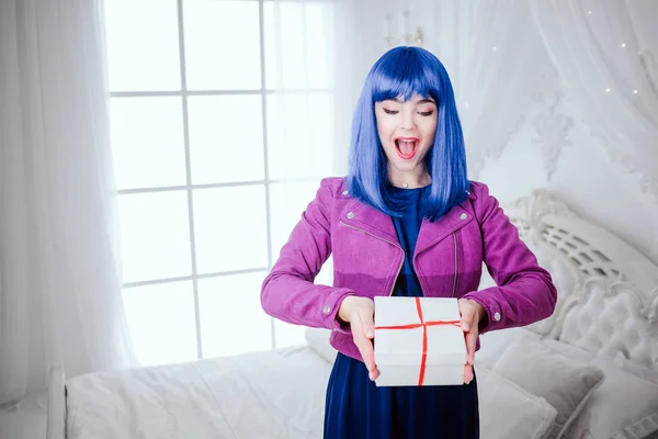 Fashionabla freak. Glamour förvånad vacker kvinna med blått hår håller gåva i vita sovrummet. Mode och skönhet koncept — Stockfoto